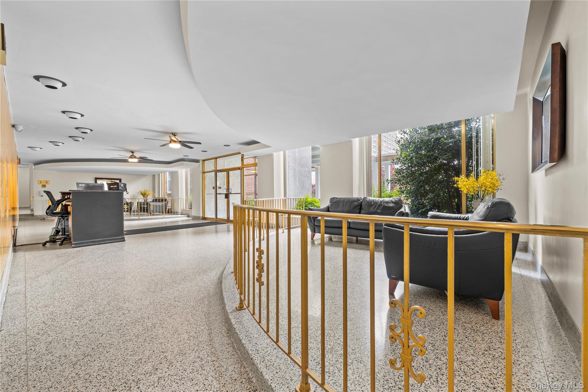 Building lobby with black leather seating, terrazzo floors, and gold railings beside large windows.