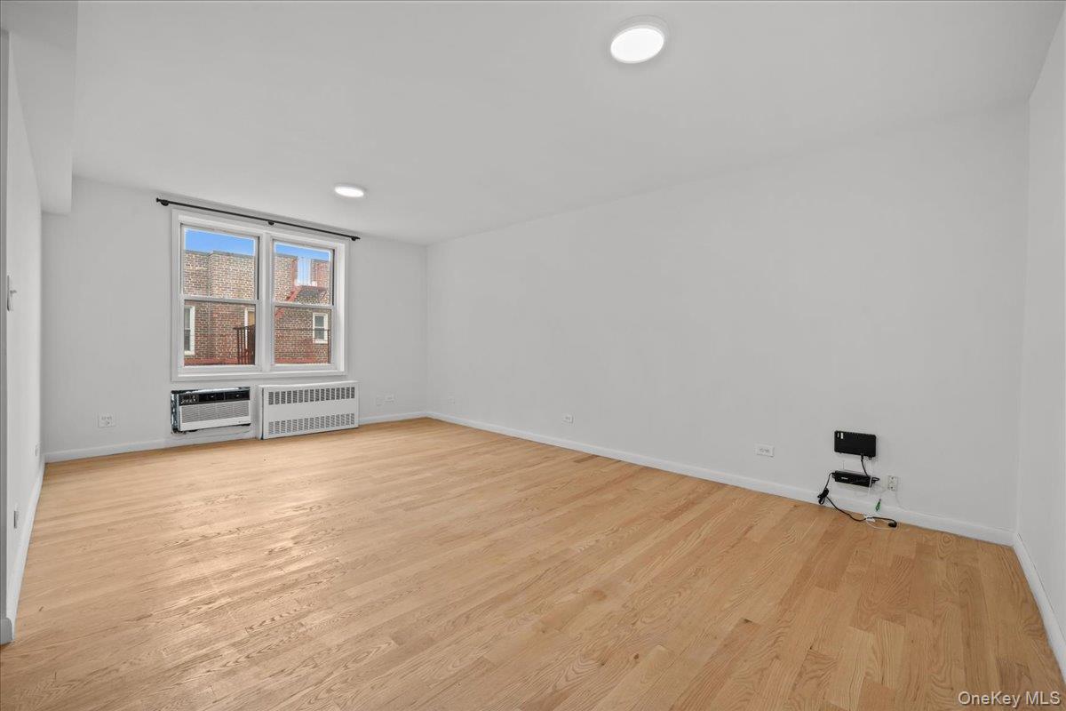 Vacant living room with hardwood floors, two windows, and a window air conditioner.