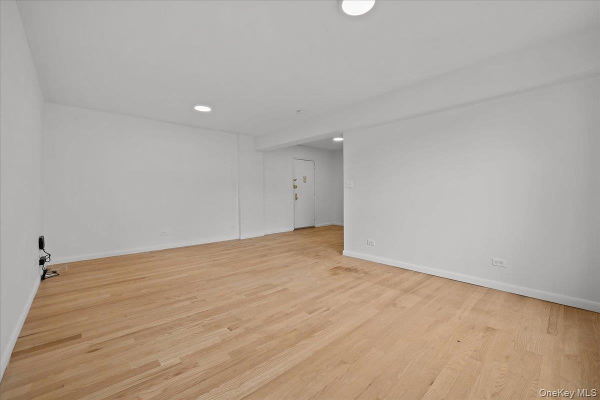 Empty living room with light hardwood floors, white walls, and recessed lighting.