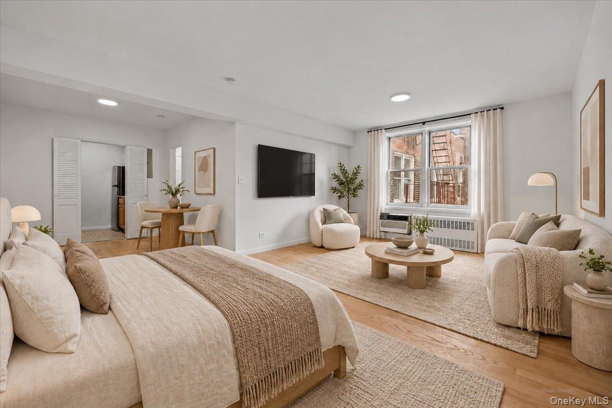 Staged apartment bedroom and living area with neutral furniture, a round coffee table, and a large curtained window.