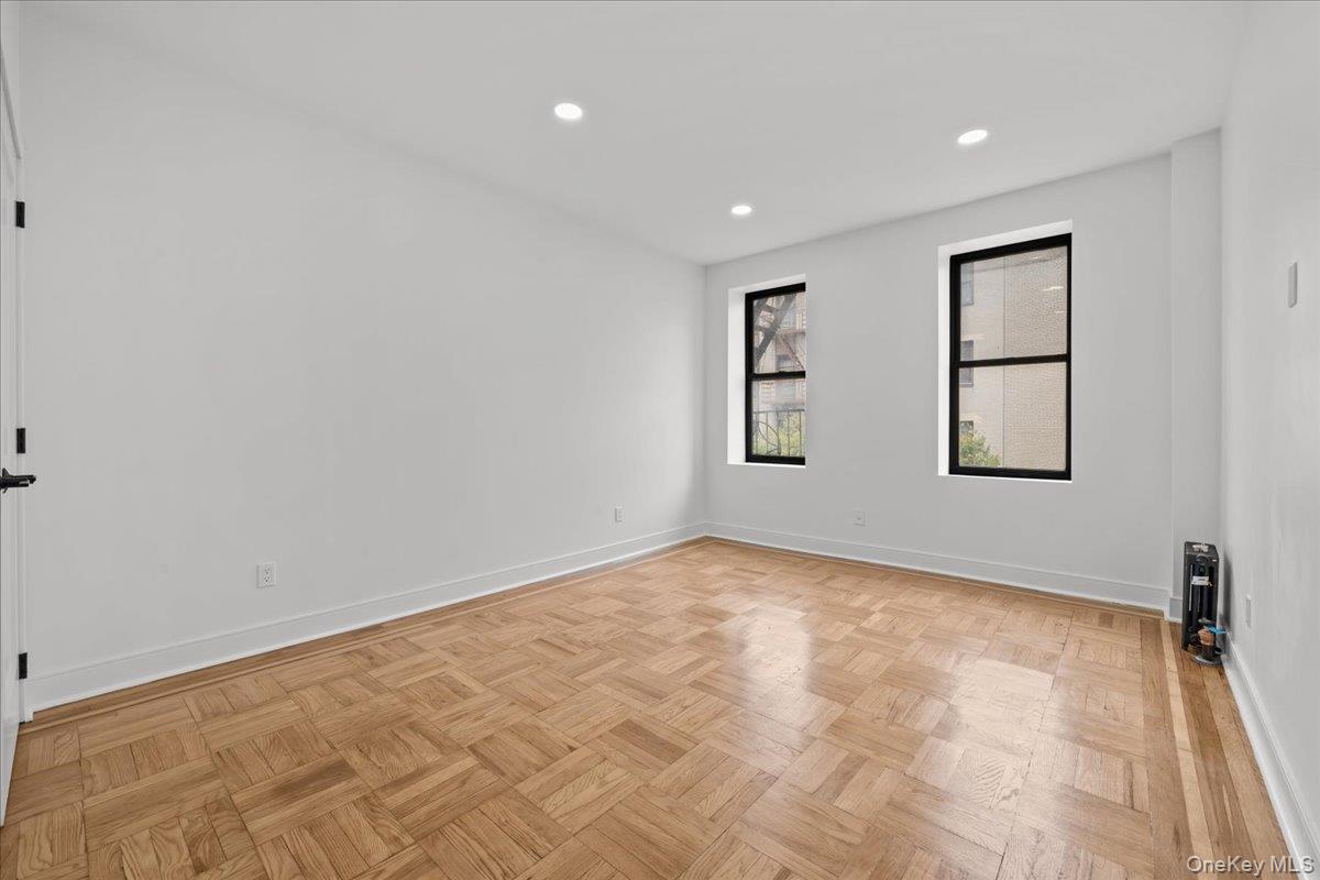 Empty room with parquet flooring, white walls, and two black-framed windows.