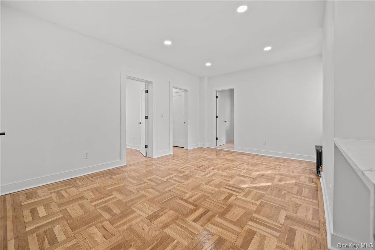 Empty living room with parquet floors, white walls, and several open doorways.