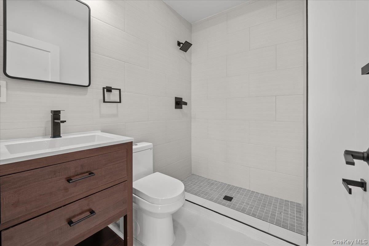 Modern bathroom with a tiled walk-in shower, dark fixtures and a wood vanity.