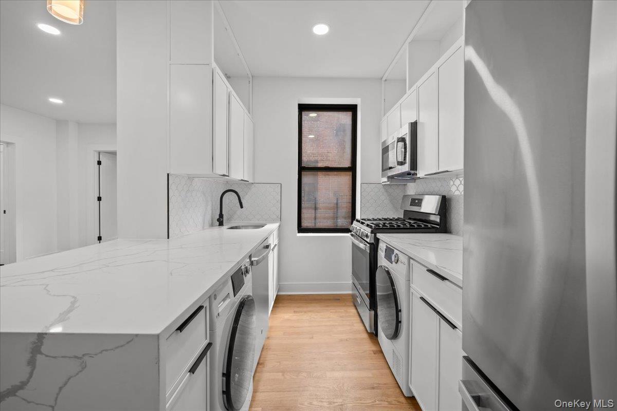 Kitchen with white cabinets, veined stone counters, gas range, and in-kitchen washer and dryer.