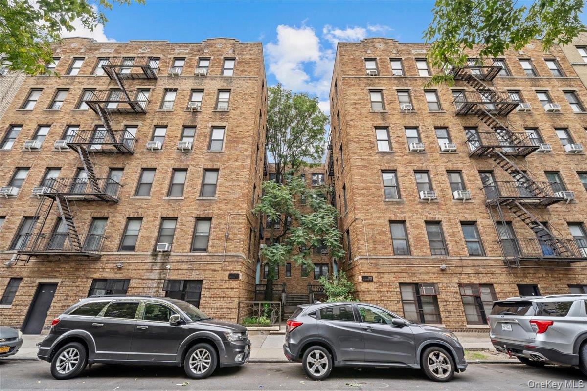 Brick apartment building with metal fire escapes and a leafy courtyard between its front wings.