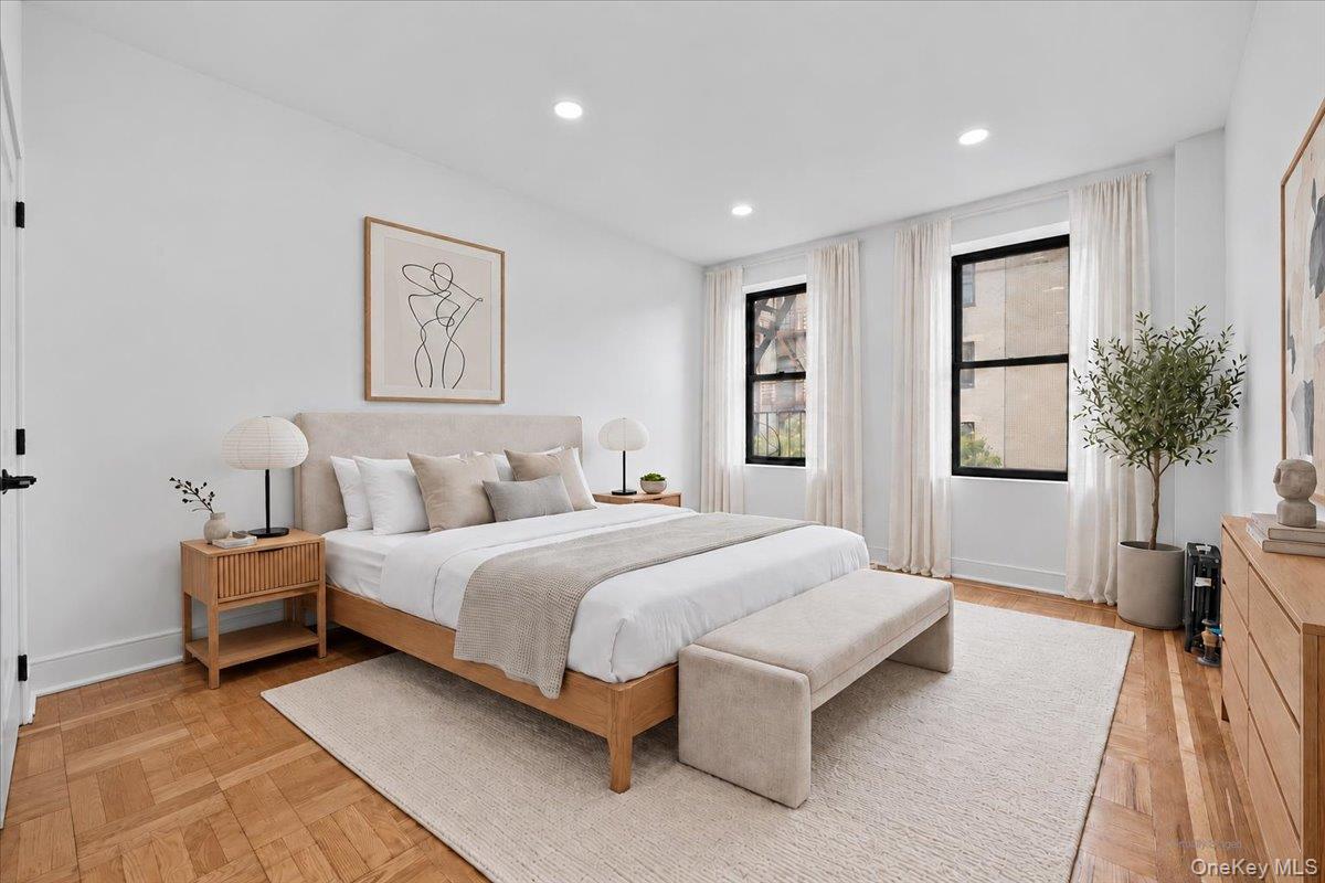 Staged bedroom with a king bed, upholstered bench, and two tall windows.