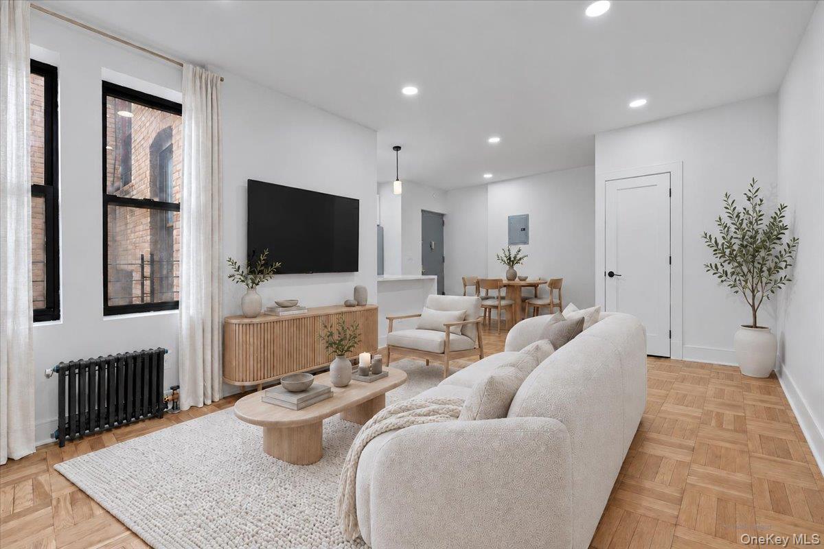 Staged living room with white sofas, tall windows, parquet floors, and an adjoining dining area.