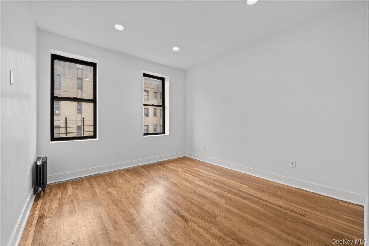 Empty apartment room with hardwood floors, two black-framed windows, and a radiator.
