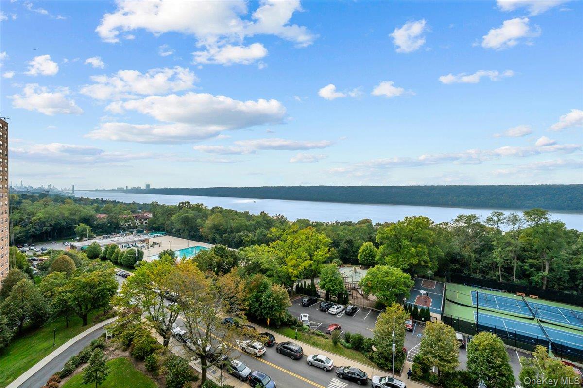 Panoramic Hudson River view with wooded shoreline, distant skyline, and tennis courts below.