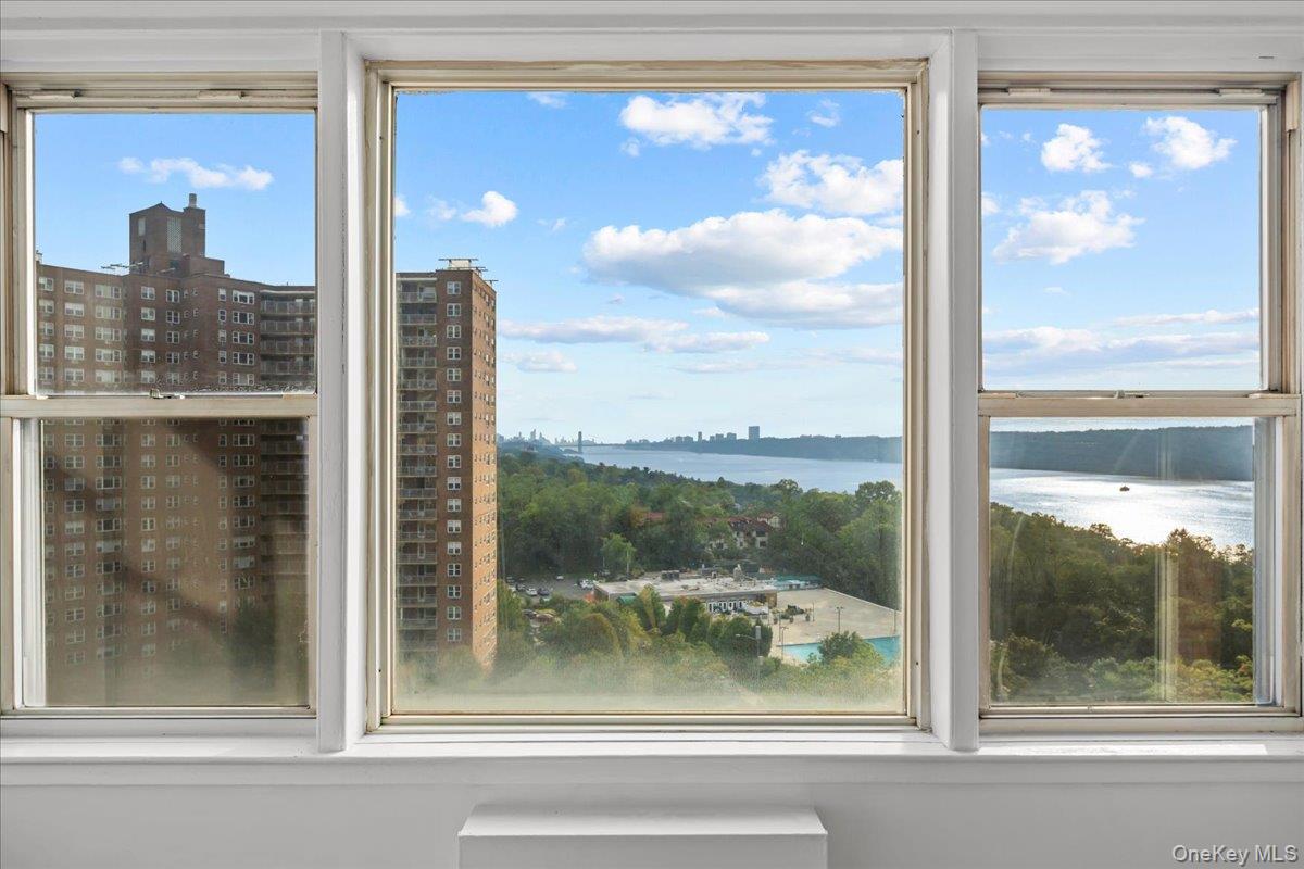Apartment windows framing a river view, wooded grounds, and a distant city skyline.
