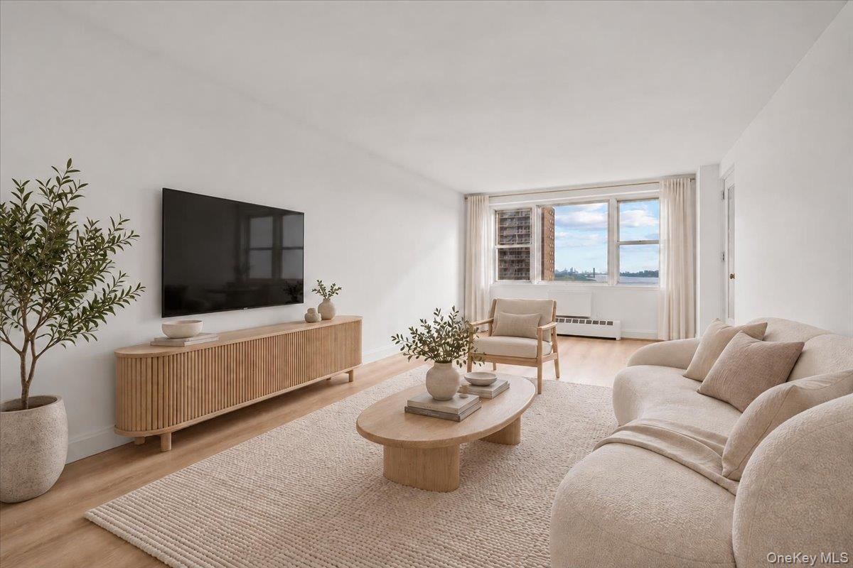 Staged living room with a cream sectional, oval wood coffee table, and large windows overlooking the skyline.