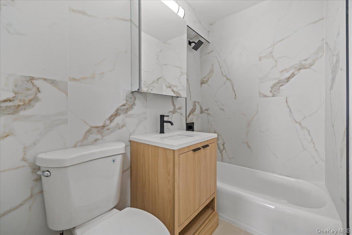 Bathroom with marble-look tile, a light wood vanity, white bathtub, and black fixtures.
