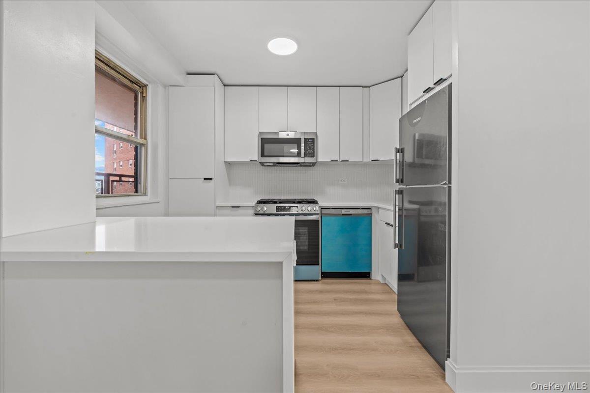 Modern white kitchen with a large peninsula, stainless steel appliances, and blue protective film on the dishwasher.