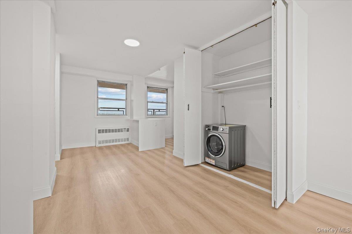 Empty apartment room with two windows and a washer and dryer in an open closet.