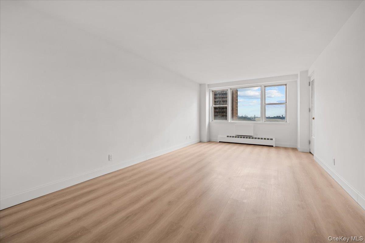 Empty apartment living room with pale wood floors and large windows overlooking the city.
