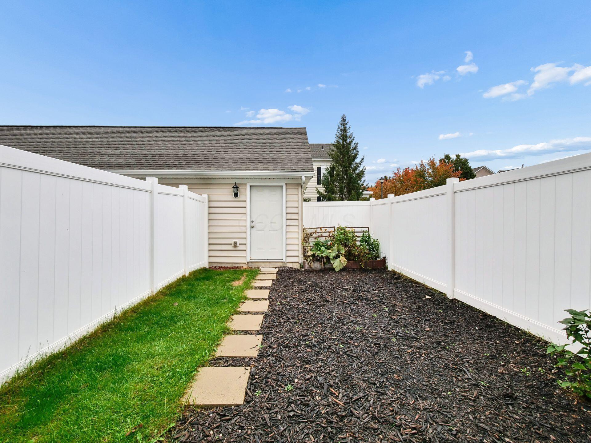 Fenced backyard with a stepping-stone path, lawn strip, mulched garden beds, and small outbuilding.