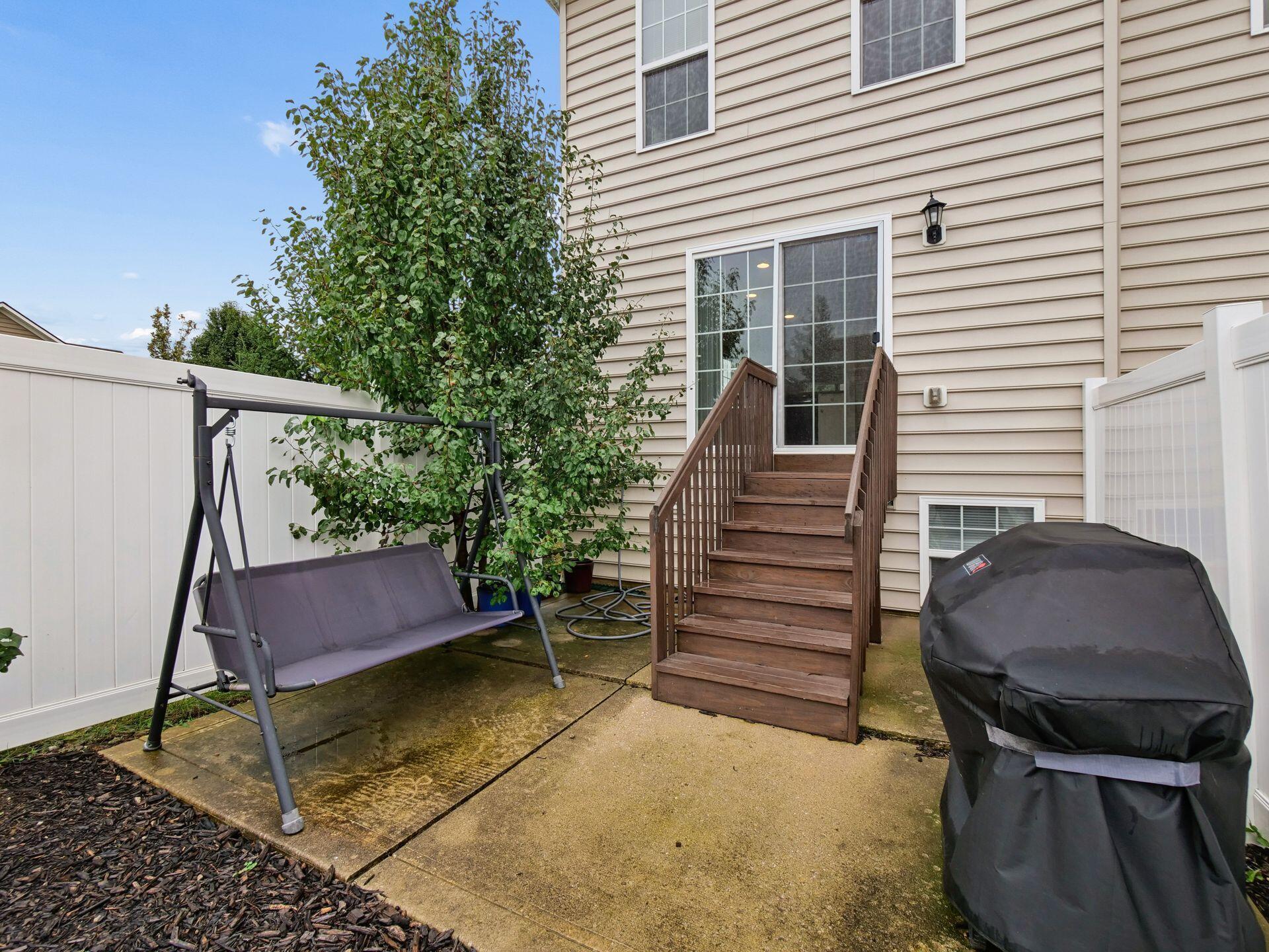 Fenced backyard patio with wooden steps, a garden swing, and a covered grill.