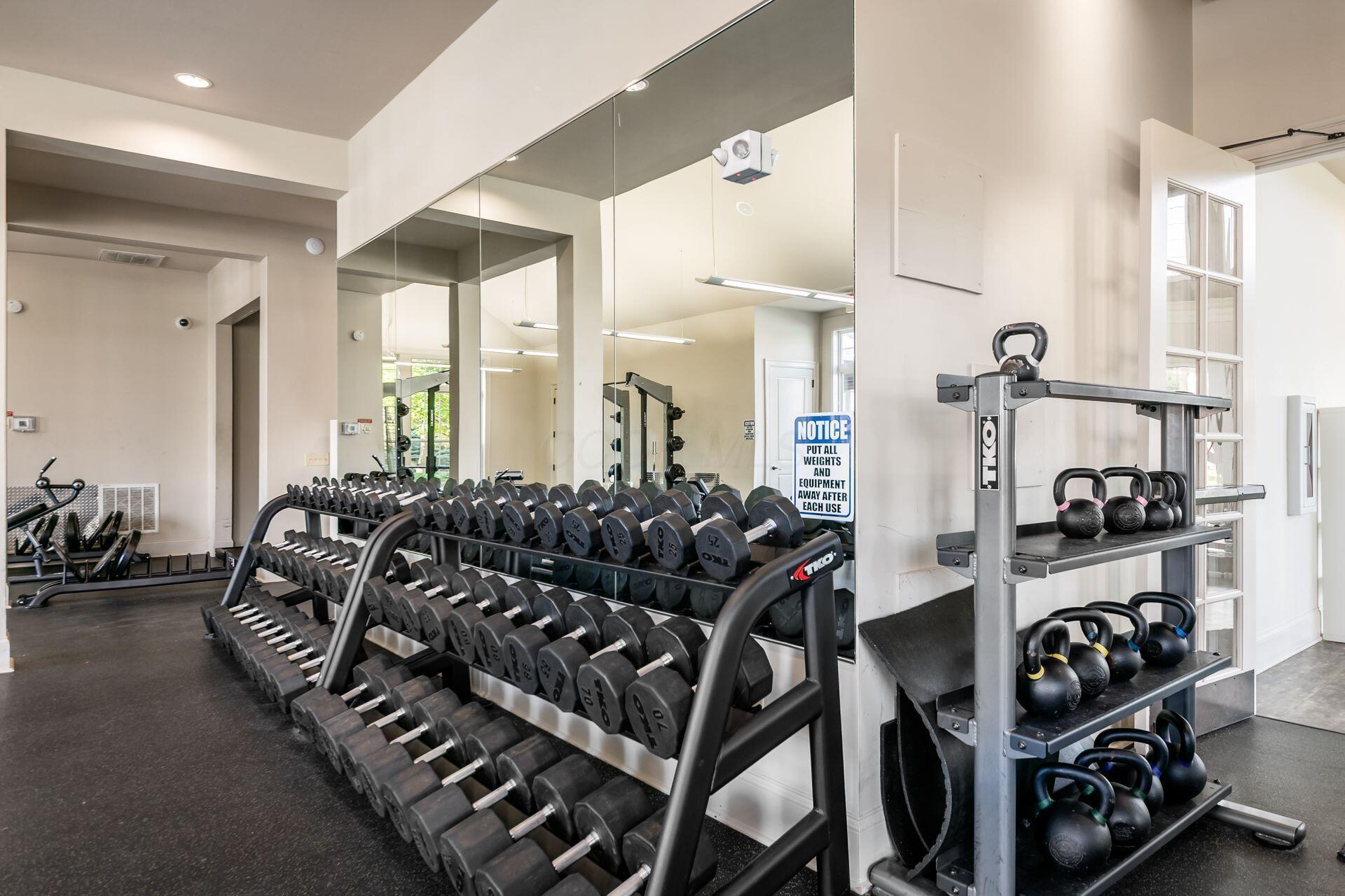 Fitness room with mirrored walls, rows of dumbbells, and kettlebells on racks.