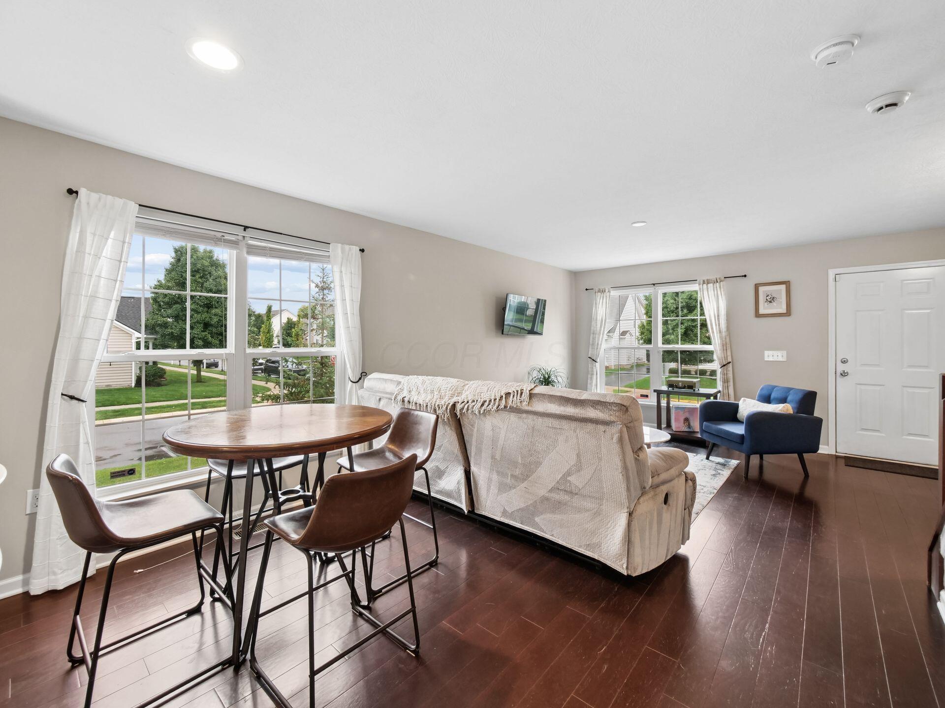 Furnished living and dining area with dark wood floors, large windows, and a blue armchair.