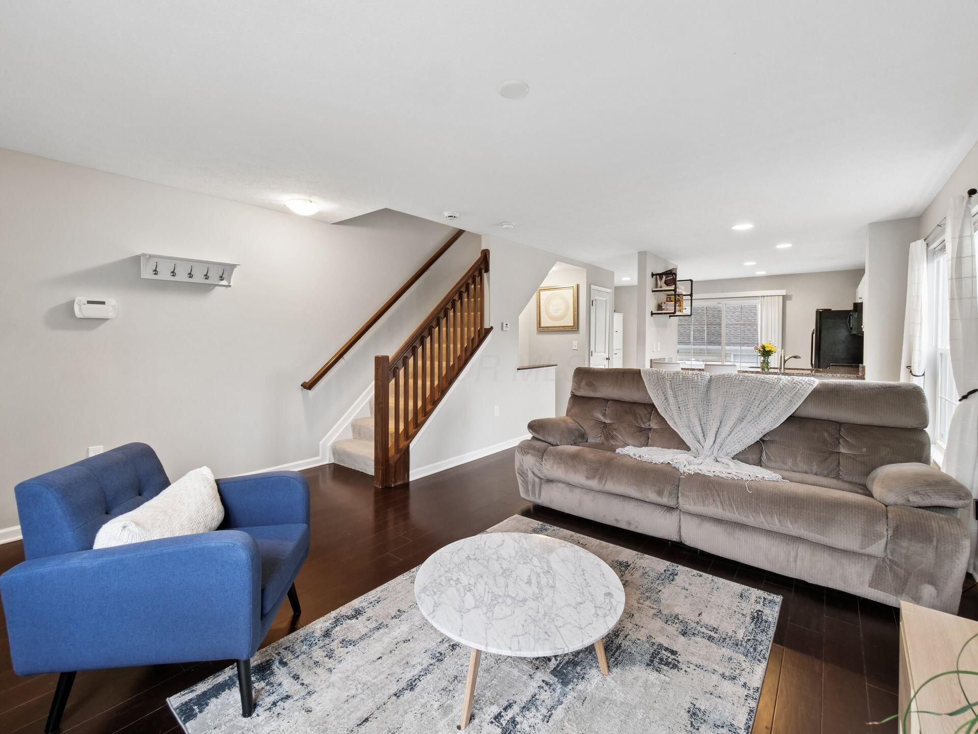 Furnished living room with a blue armchair, gray sofa, dark hardwood floors, and a staircase.