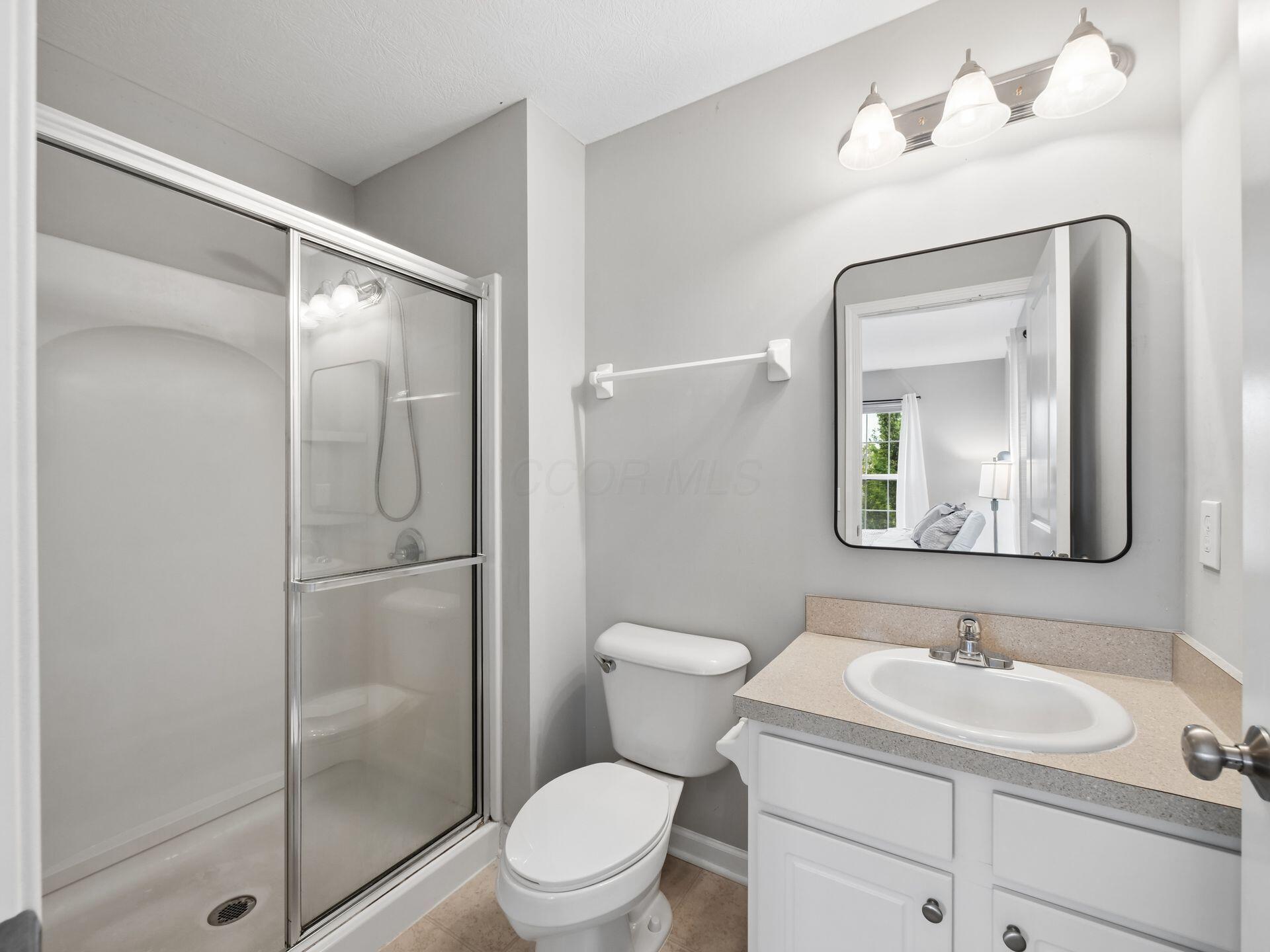 Bathroom with glass shower, toilet, and white vanity beneath a large black-framed mirror.