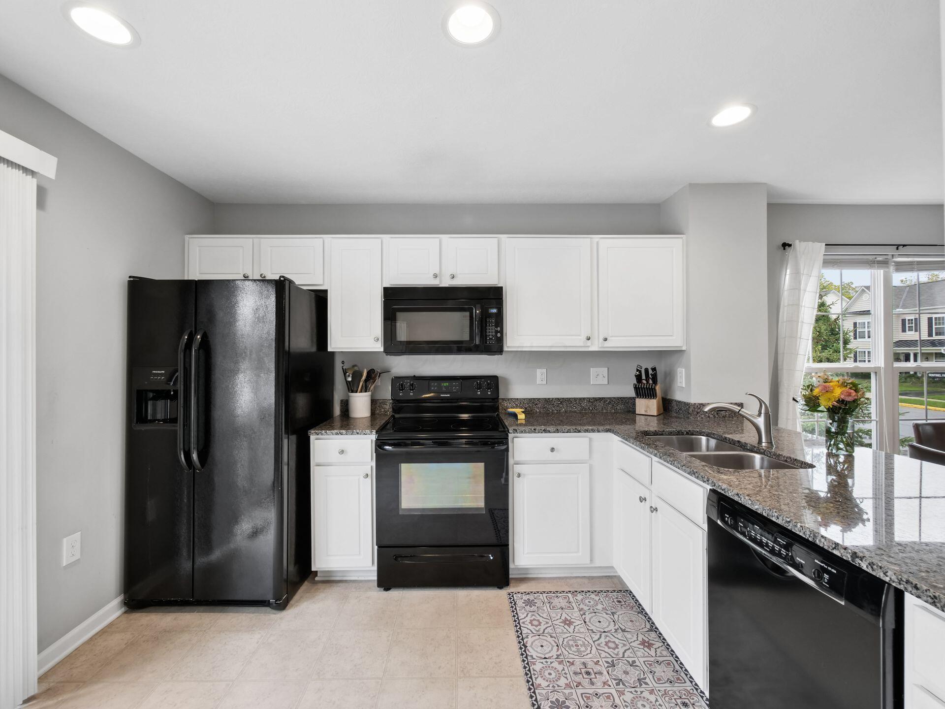 Kitchen with white cabinetry, black appliances, granite counters, and a window above the double sink.