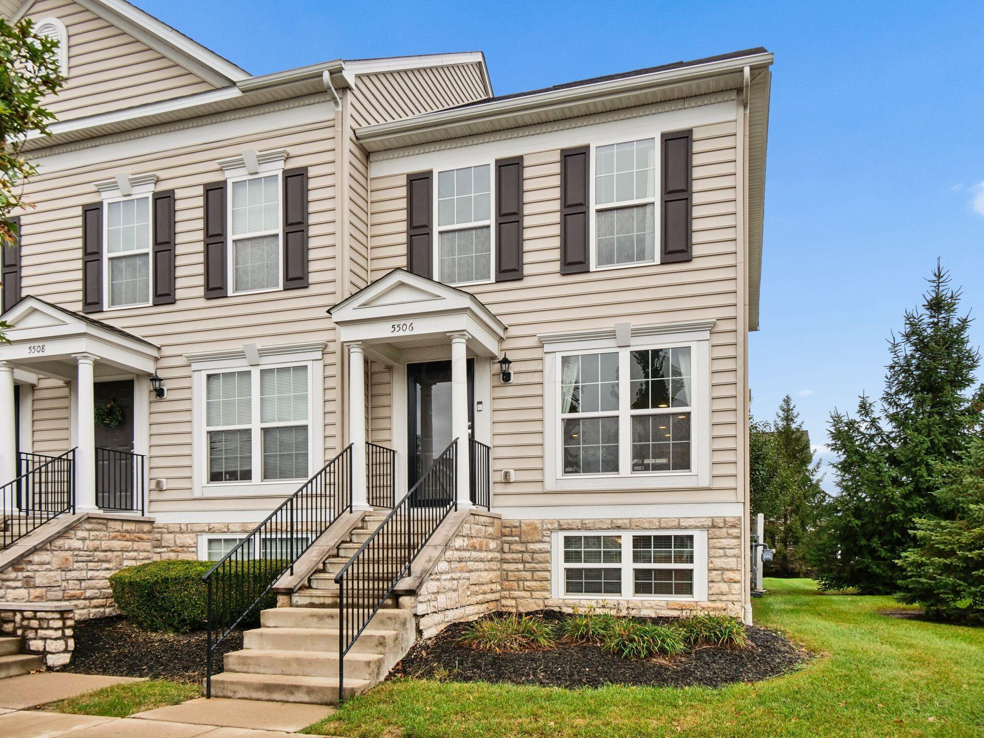 Townhouse exterior with stone veneer, beige siding, and raised entry steps with black railings.