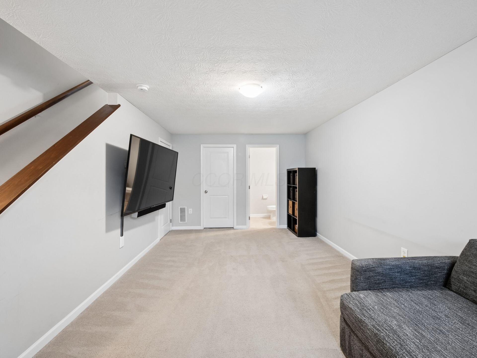 Carpeted living room with a wall-mounted TV beneath the staircase and a gray sofa.