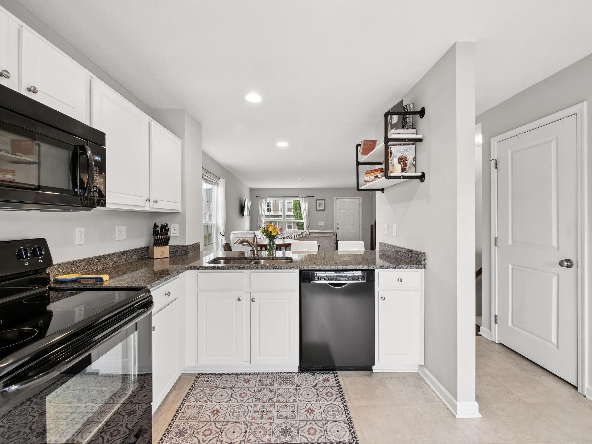 Kitchen with white cabinets, dark granite counters, black appliances, and a patterned tile rug.