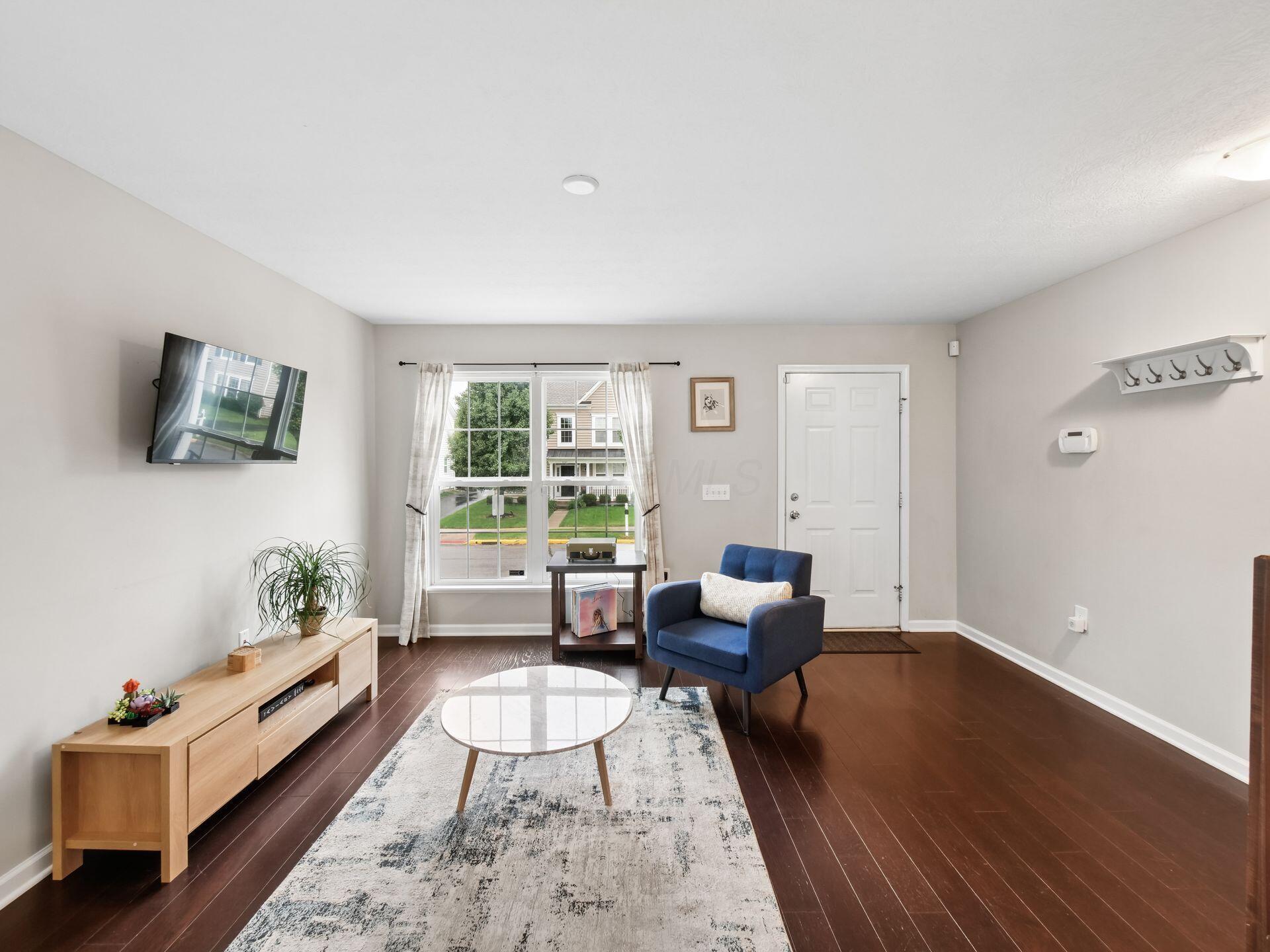 Living room with a blue armchair, oval coffee table, and large curtained window.