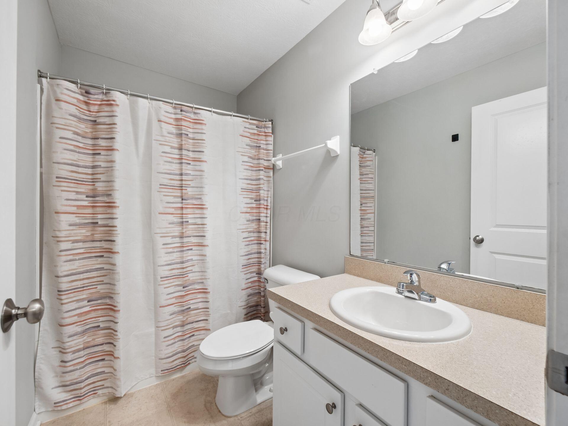 Bathroom with a white vanity and large mirror beside a toilet and striped shower curtain.