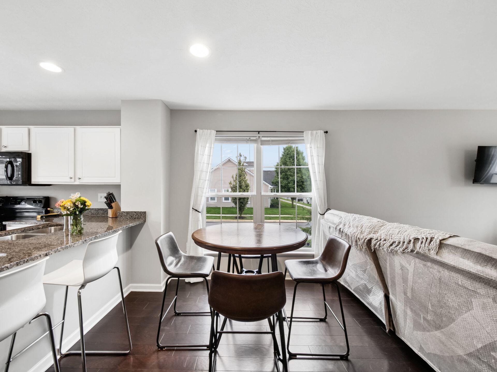Dining area with a round table by a curtained window, open to the kitchen and living room.