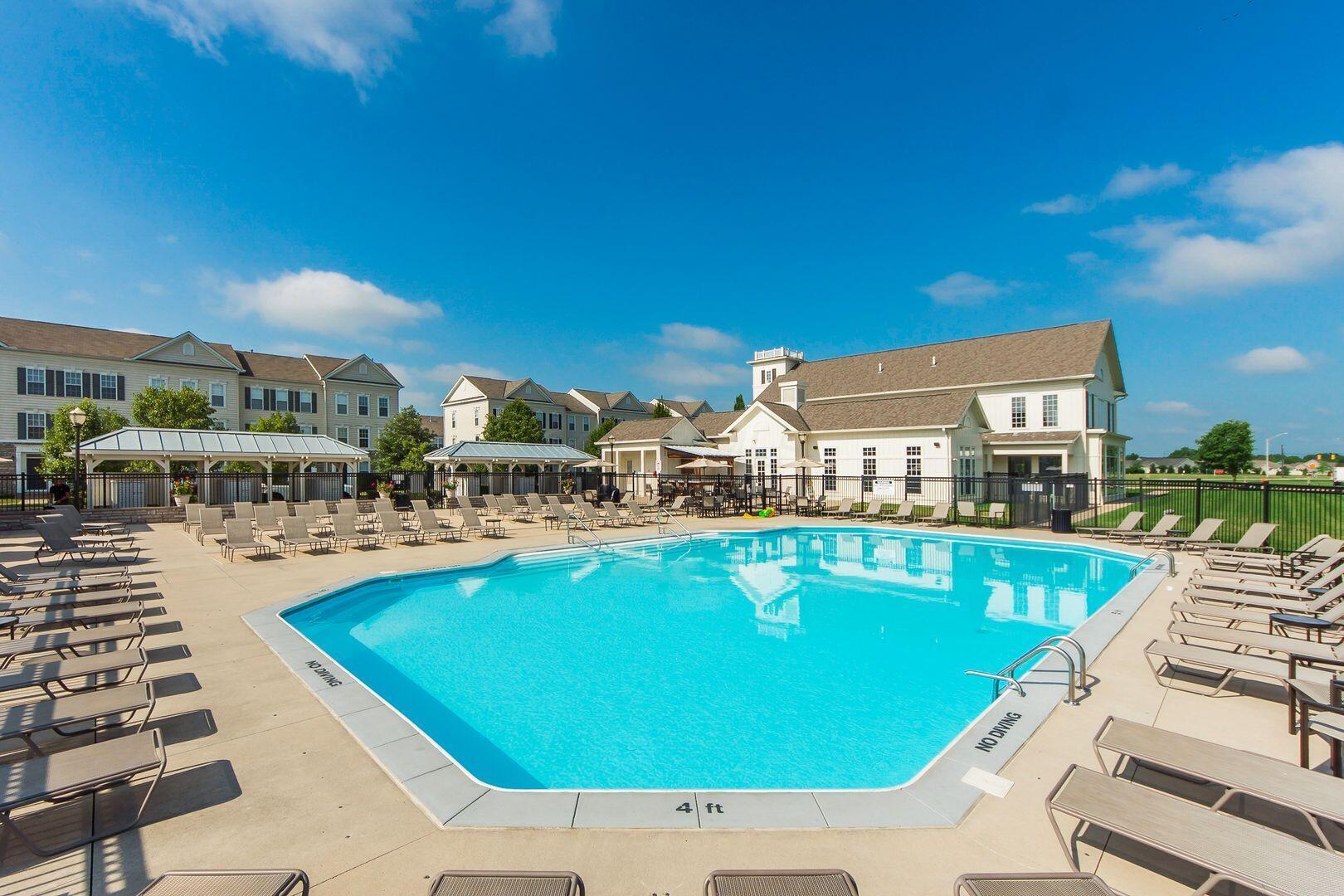 Community pool with lounge chairs, a clubhouse, and residential buildings in the background.