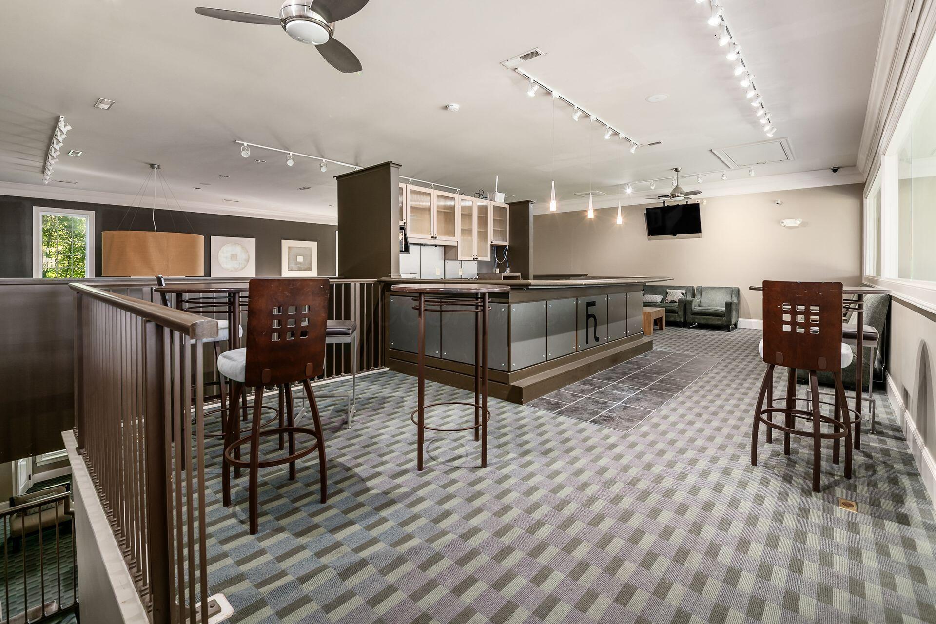 Communal lounge with a long bar counter, tall stools, patterned carpet, and seating.