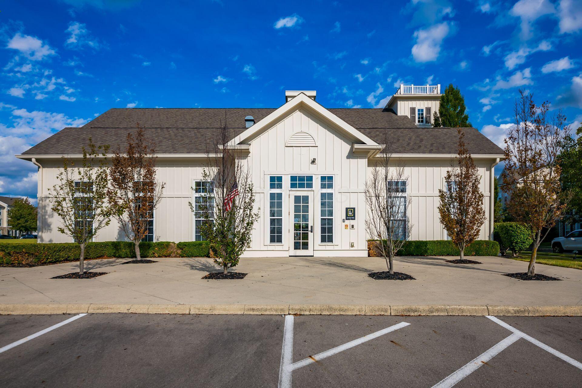 White building with a central gable, tall entrance windows, and a paved parking area.