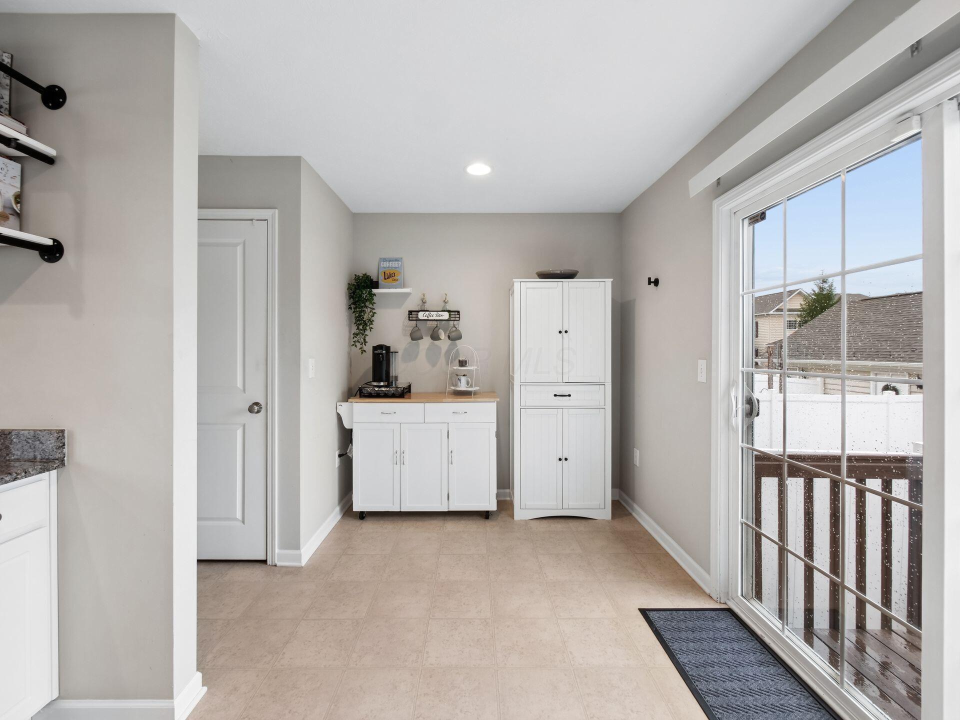 Tiled room with a coffee bar and white cabinets beside a sliding glass door overlooking a snowy deck.