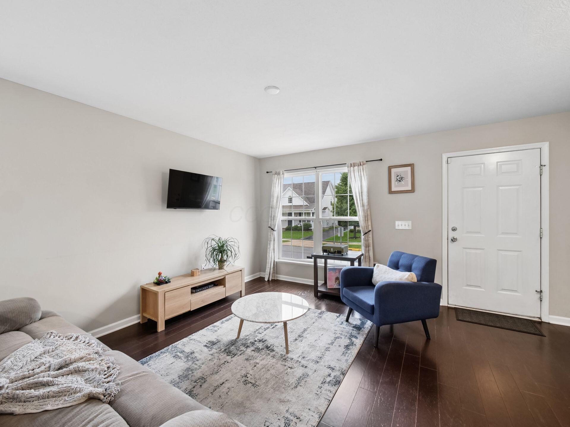 Furnished living room with a blue armchair, round coffee table, and window overlooking neighboring homes.