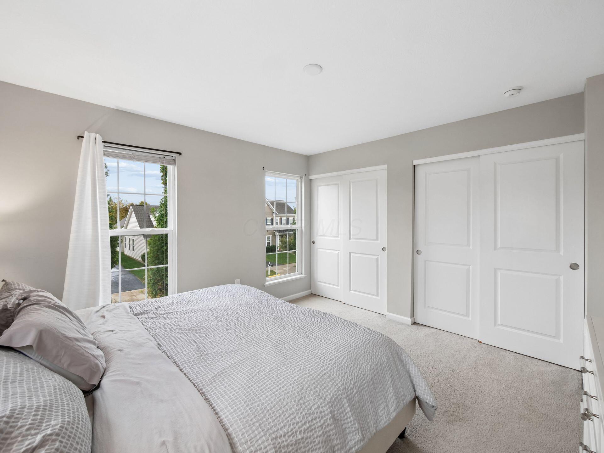 Bedroom with a neatly made bed, two windows, and white sliding closet doors.