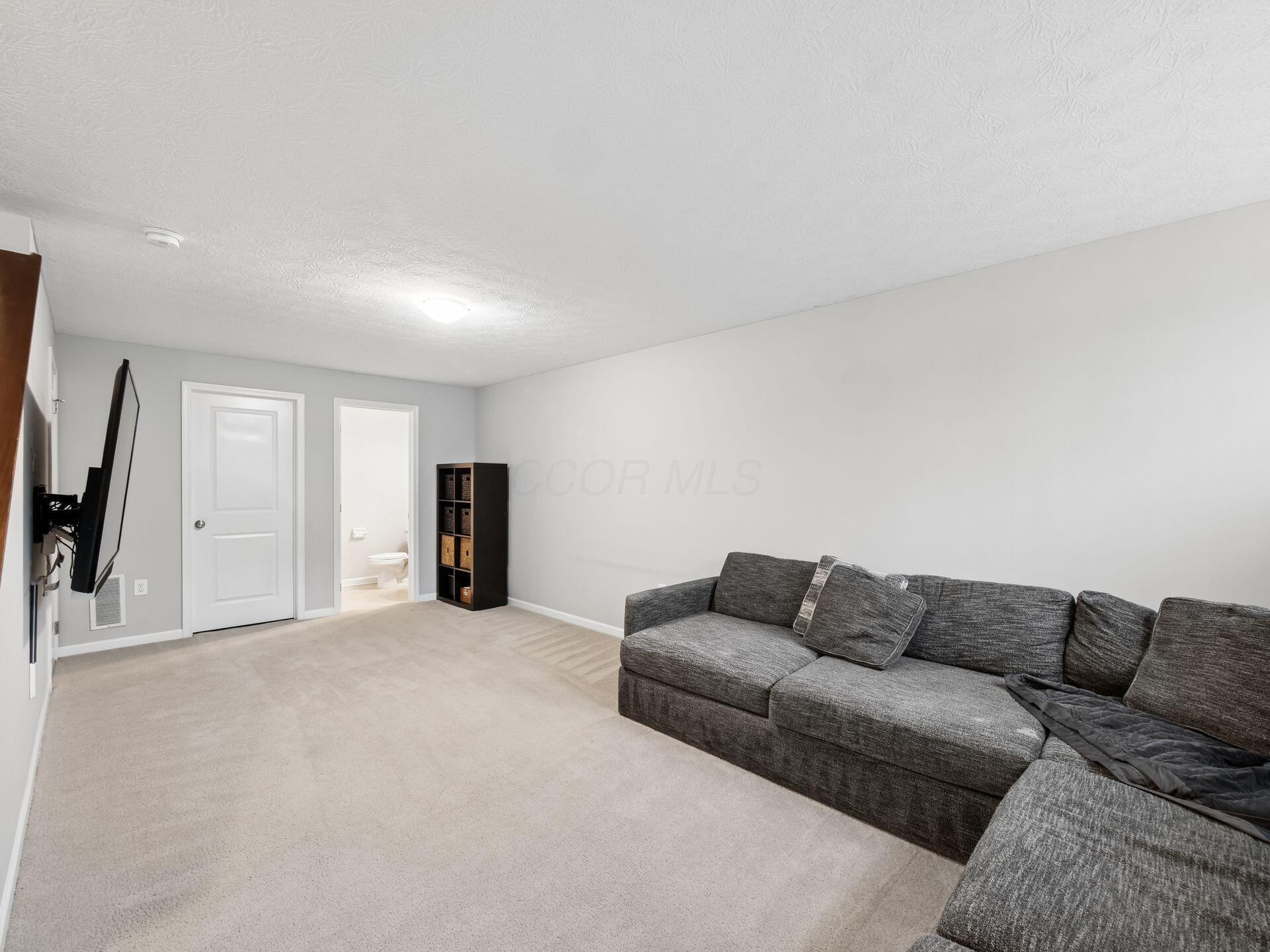 Living room with a large gray sectional, wall-mounted television, and open doorway to a bathroom.