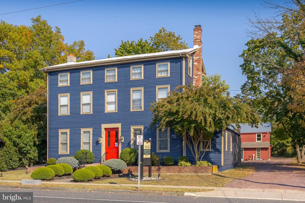 Blue three-story building with a bright red front door, trimmed shrubs, and a brick chimney.
