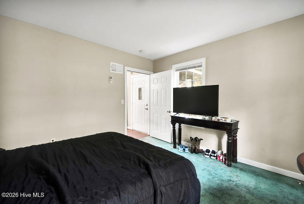 Bedroom with a black-covered bed, turquoise carpet, and television beside an open door.