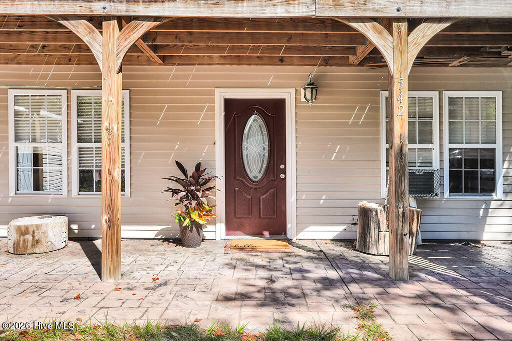 Home entrance with a burgundy oval-glass door beneath a timber-covered porch.