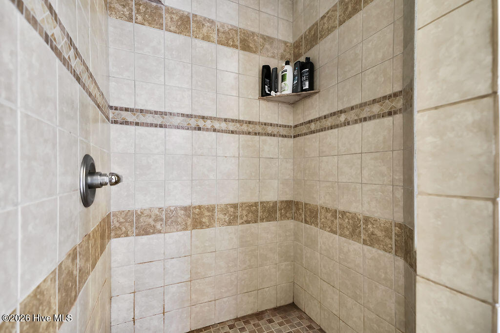 Tiled shower with decorative brown bands, chrome control, and toiletries on a corner shelf.