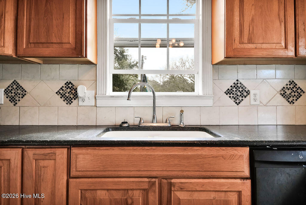 Kitchen sink beneath a large window, with warm wood cabinets and a cream tile backsplash.