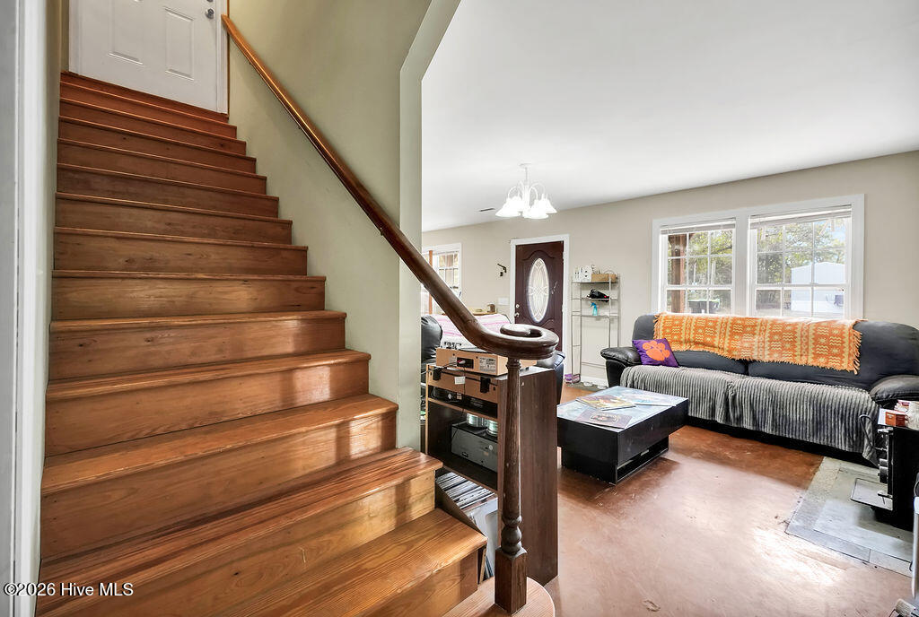 Living room with a broad wooden staircase, dark sofa, and large windows.