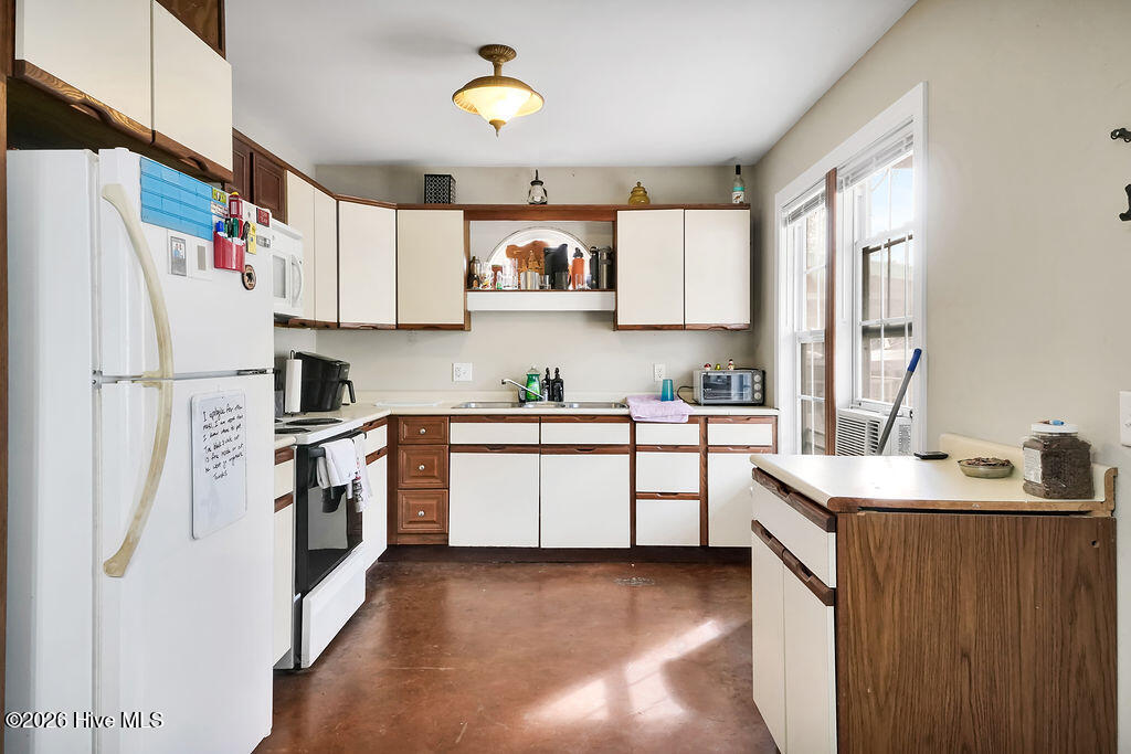 Kitchen with cream and dark wood cabinets, white appliances, and tall daylight-filled windows.