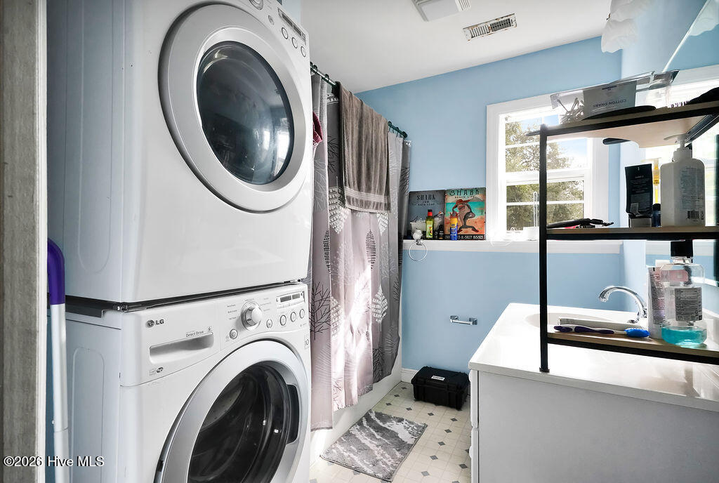 Bathroom with blue walls, a glass shower screen, white vanity, and stacked washer and dryer.