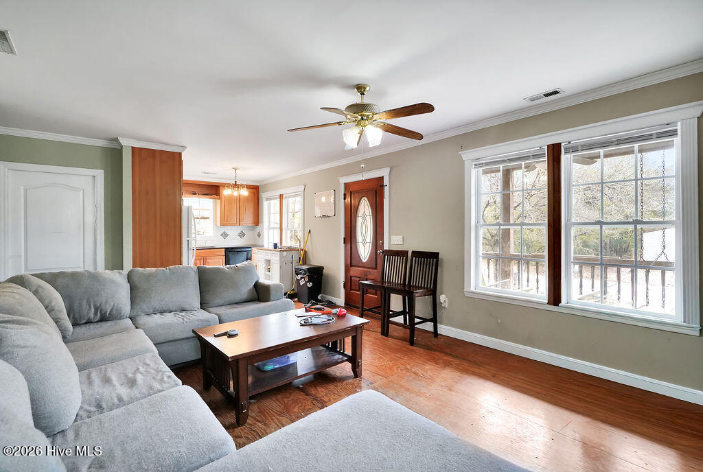 Living room with gray sectional, wood floors, and large windows beside an open kitchen.