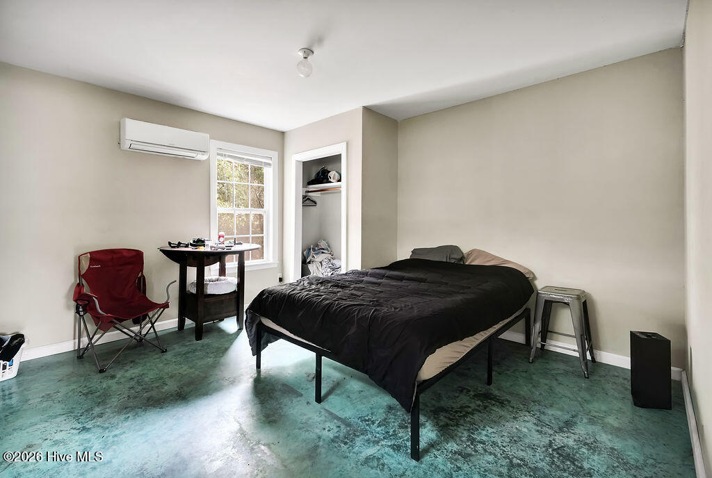 Bedroom with a black-covered bed, green concrete floor, and wall-mounted air conditioner.