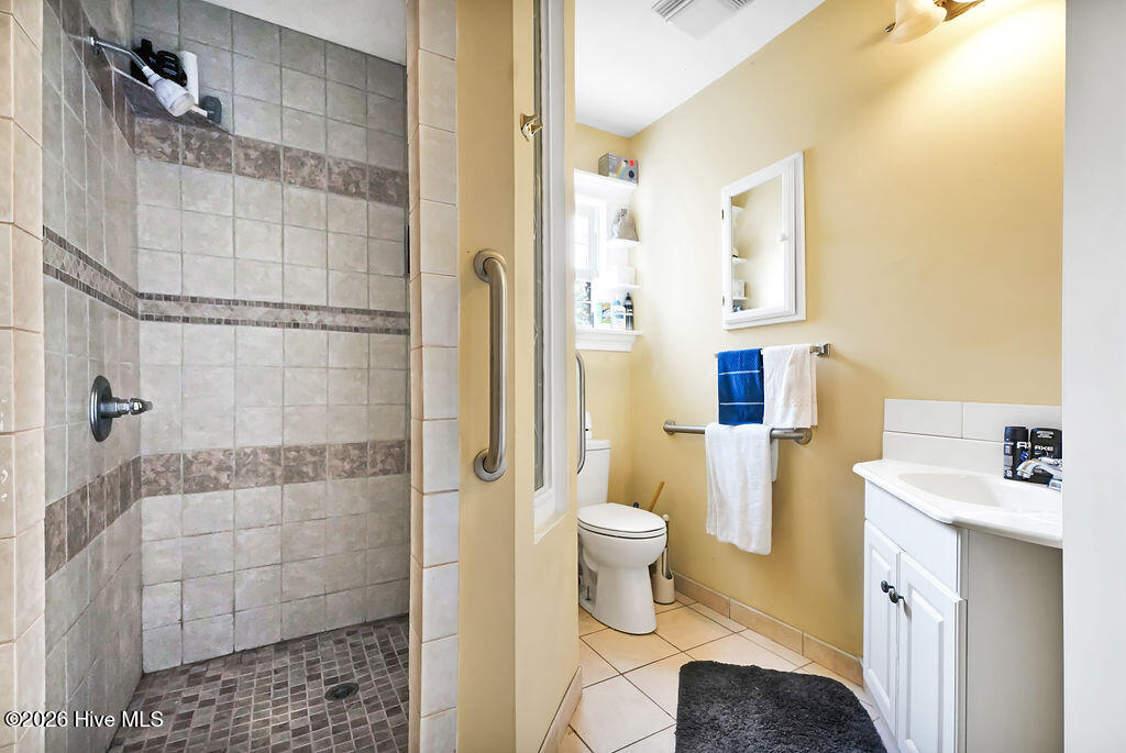 Bathroom with a tiled walk-in shower, grab bars, toilet, and white vanity.